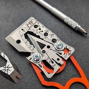 Könnte beinhalten: Ein silbernes Multitool mit rotem Griff. Das Werkzeug hat eine Vielzahl von Funktionen, darunter ein Lineal, ein Flaschenöffner, ein Messer und ein Schraubendreher. Das Werkzeug ist mit "MRF Adventure" beschriftet.