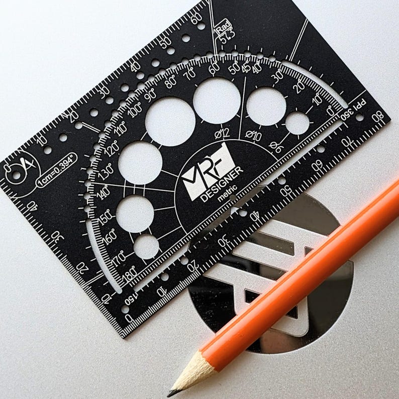 May include: A black rectangular drafting tool with white markings, including a protractor, circular cutouts, and the text MRF DESIGNER metric. An orange pencil with a sharpened lead tip is positioned diagonally across the tool.