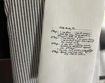 May include: A white tea towel with a handwritten recipe for "Natty Buddy Pie" on it. The recipe includes ingredients like flour, pecans, butter, cream cheese, and powdered sugar. The recipe is written in cursive.