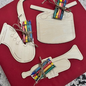 Puede incluir: Recortes de madera de un saxof&oacute;n, un tambor y una trompeta, cada uno con un paquete de crayones de colores atados con hilo. Los art&iacute;culos est&aacute;n dispuestos sobre una superficie roja.