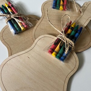 Puede incluir: Plantillas de manualidades de madera con forma de guitarra con paquetes de crayones. Cada plantilla est&aacute; hecha de madera de color claro con un contorno oscuro. Los crayones est&aacute;n en pl&aacute;stico transparente, atados con hilo, e incluyen crayones rojos, amarillos, verdes y azules.