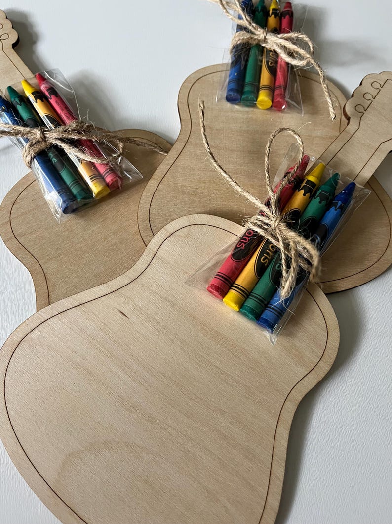 Puede incluir: Plantillas de manualidades de madera con forma de guitarra con paquetes de crayones. Cada plantilla est&aacute; hecha de madera de color claro con un contorno oscuro. Los crayones est&aacute;n en pl&aacute;stico transparente, atados con hilo, e incluyen crayones rojos, amarillos, verdes y azules.