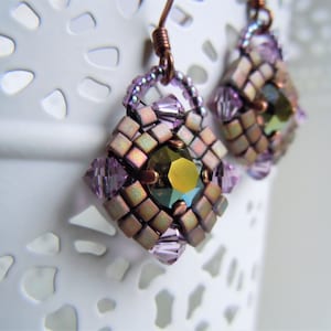 Peut inclure: Une paire de boucles d'oreilles de forme carrée, avec des perles iridescentes violettes et cuivrées, et une grosse pierre précieuse verte au centre.
