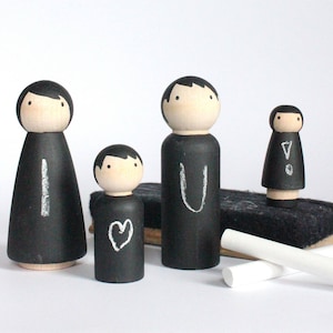 May include: Four black wooden peg dolls with chalkboard faces. The dolls are standing on a black chalkboard eraser. The dolls have the letters 'I', 'U', and '!' written on them. The smallest doll has a heart drawn on it.