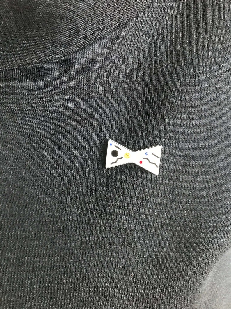 May include: White bow tie pin with black, blue, red, and yellow paint splatter design.