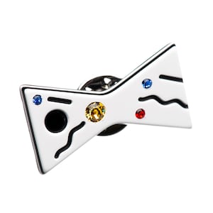 May include: White bow tie pin with black lines and colorful rhinestones. The pin has a black circle in the center.
