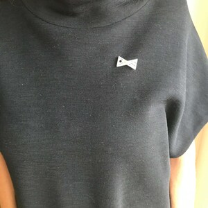 May include: A black mock neck shirt with a small white bow brooch with a yellow center.