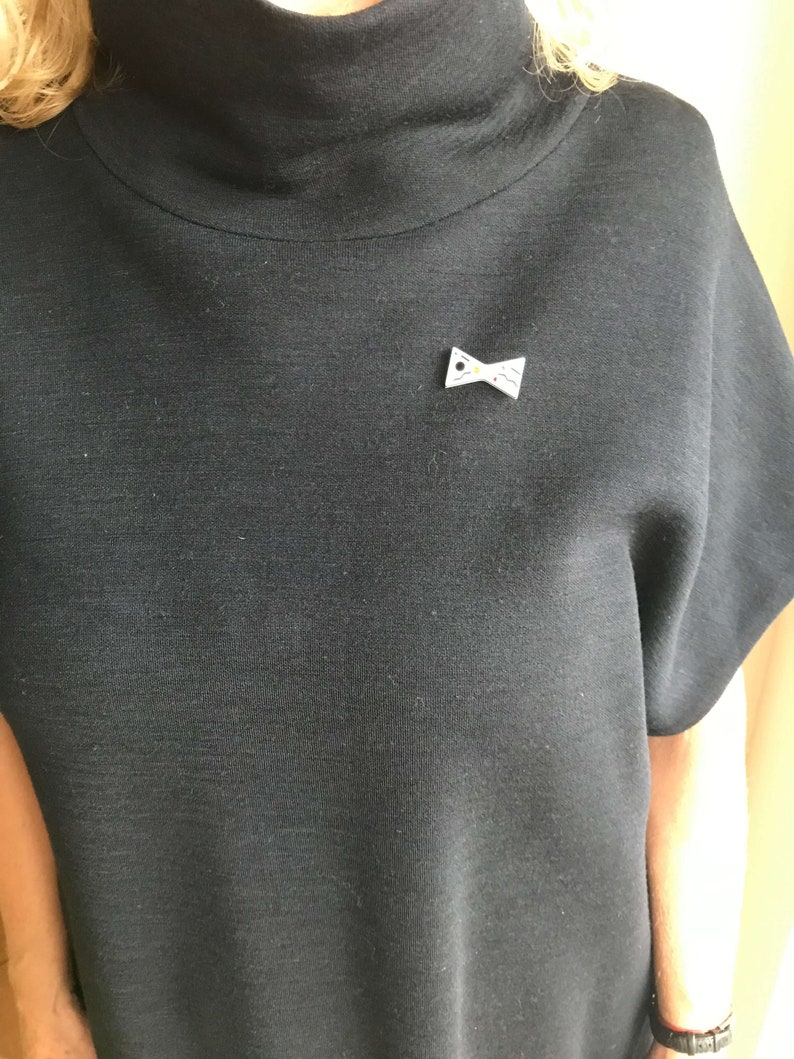 May include: A black mock neck shirt with a small white bow brooch with a yellow center.