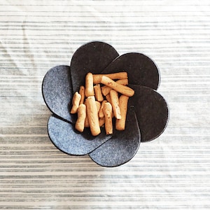 May include: A gray felt flower-shaped bowl filled with a pile of thin, crispy breadsticks.