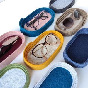 May include: Assortment of felt eyeglass holders in various colors, including teal, yellow, burgundy, gray, and blue. Each holder features a soft felt lining and a rounded oval shape.