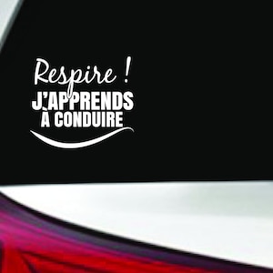 Puede incluir: Una pegatina de vinilo blanco en la ventana trasera de un coche. La pegatina dice "Respire! J'apprends a conduire", que se traduce como "¡Respira! Estoy aprendiendo a conducir".