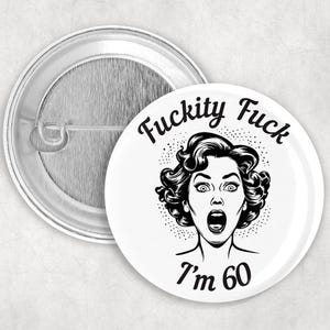 May include: A white button with black text that reads "F*ckity F*ck I'm 60". A black and white illustration of a woman with a surprised expression is in the center of the button.