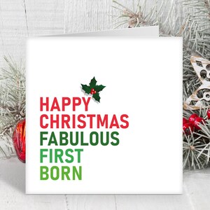 May include: A white Christmas card with green holly and red berries at the top. The text reads "Happy Christmas Fabulous First Born" in red and green.
