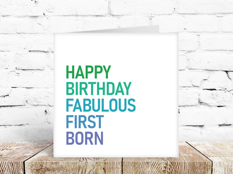 May include: A white card with the text "HAPPY BIRTHDAY FABULOUS FIRST BORN" in a gradient of green, blue, and purple.