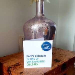 Op de afbeelding: Een witte kaart met de tekst "Happy Birthday to one of our favourite children" en een blauwe knop met de tekst "Five star son would recommend" en vijf sterren.