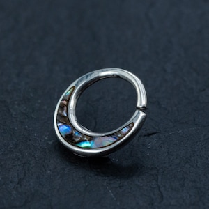 Puede incluir: Un aro de plata para la oreja con una incrustación en forma de media luna de nácar de abulón iridiscente.