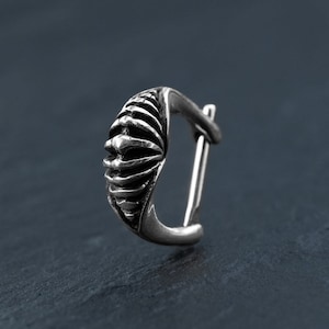 May include: A silver hoop earring with a textured, geometric design. The earring is made of metal and has a hinged closure.