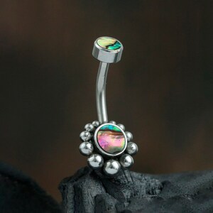 May include: A silver belly button ring with a round iridescent abalone shell top and a cluster of silver beads around the bottom.