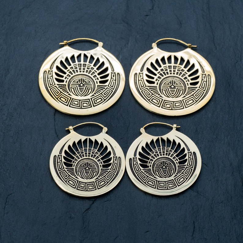 Puede incluir: Cuatro pendientes de aro dorados con un dise&ntilde;o geom&eacute;trico. Cada pendiente presenta un patr&oacute;n circular con un s&iacute;mbolo central en forma de sol y un borde repetitivo.
