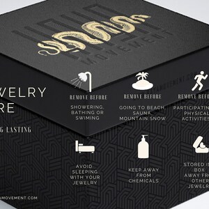 May include: Black box with gold lettering that reads "Kaya Movement". The box has a graphic of a snake and instructions for jewelry care. The instructions include removing jewelry before showering, bathing, swimming, going to the beach, sauna, mountain snow, or participating in physical activities. The instructions also include avoiding sleeping with jewelry, keeping jewelry away from chemicals, and storing jewelry in a box away from other jewelry.