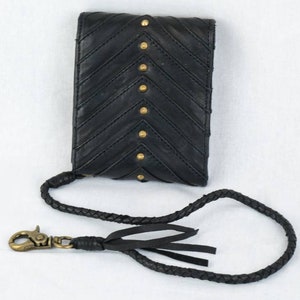 Pode incluir: Capa de telefone de couro preto com padr&atilde;o chevron e tachas douradas. A capa tem uma al&ccedil;a tran&ccedil;ada preta com uma borla.