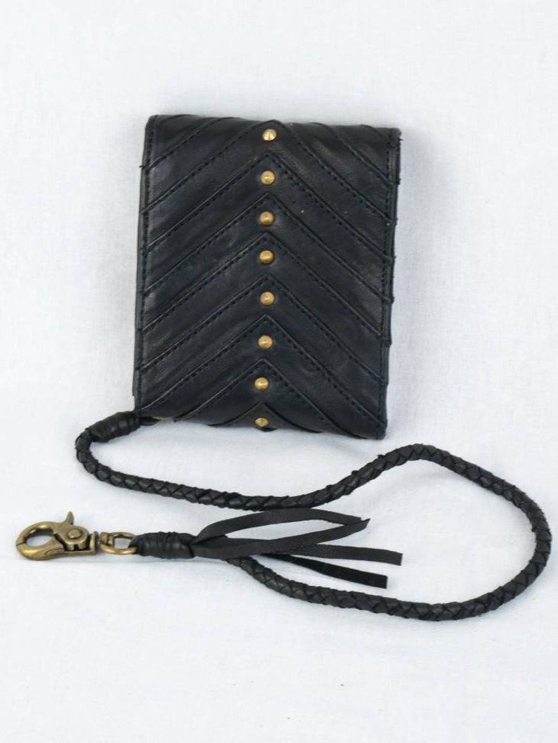 Pode incluir: Capa de telefone de couro preto com padr&atilde;o chevron e tachas douradas. A capa tem uma al&ccedil;a tran&ccedil;ada preta com uma borla.