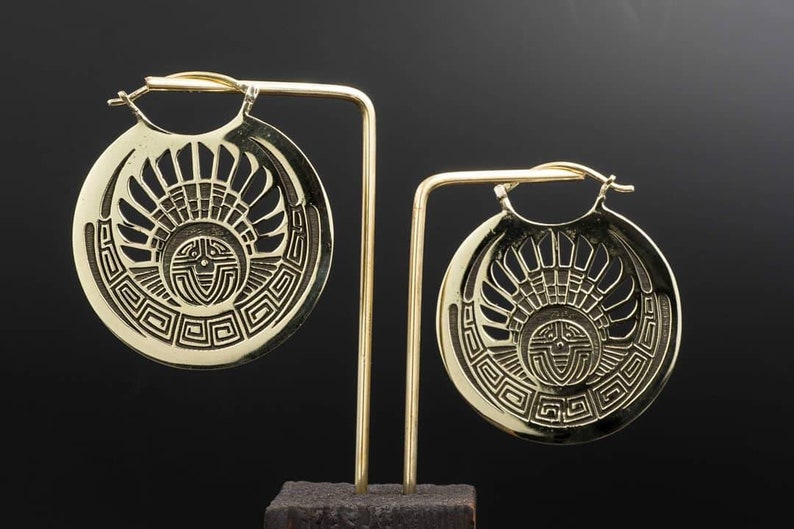 Puede incluir: Un par de pendientes de aro de oro con un dise&ntilde;o geom&eacute;trico detallado. Los pendientes se muestran en un soporte negro.