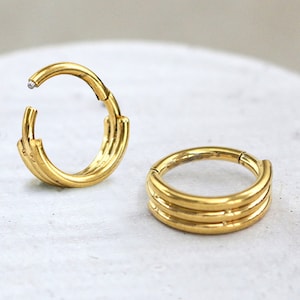 Peut inclure: Deux boucles d'oreilles à clic en acier inoxydable couleur or avec un design triple couche. Les boucles d'oreilles sont circulaires et ont un aspect sans couture.