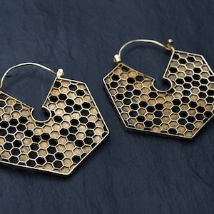 以下が含まれることがあります： ハニカムデザインのゴールドトーンのフープイヤリングのペア。イヤリングは大きく、幾何学的な形をしています。