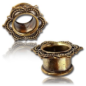 Könnte beinhalten: Zwei antik-messingfarbene Ohr-Dehnstäbe mit floralem Design. Die Dehnstäbe haben eine zylindrische Form mit ausgestelltem Boden und einem dekorativen, mehrschichtigen Blumenmuster am äußeren Rand. Das Design umfasst kleine, erhabene Punkte.