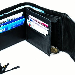 Pode incluir: Uma carteira de couro preta com fecho de correr e uma correia de couro tran&ccedil;ada. A carteira est&aacute; aberta e mostra v&aacute;rios cart&otilde;es de cr&eacute;dito e uma moeda no seu interior.
