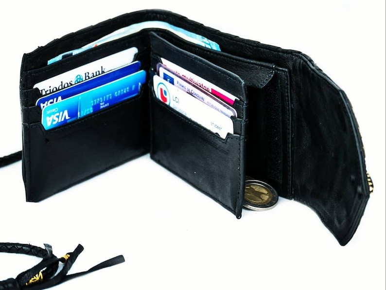Pode incluir: Uma carteira de couro preta com fecho de correr e uma correia de couro tran&ccedil;ada. A carteira est&aacute; aberta e mostra v&aacute;rios cart&otilde;es de cr&eacute;dito e uma moeda no seu interior.