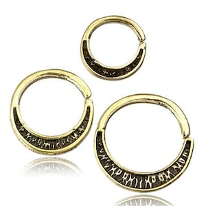 Peut inclure: Trois boucles d'oreilles en forme de cercle dorées avec une inscription noire sur le bord. L'inscription est en alphabet runique.