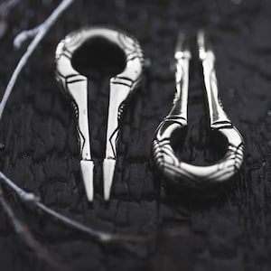 Puede incluir: Dos diapasones de metal plateados con diseños intrincados sobre un fondo negro.