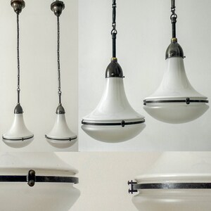 Op de afbeelding: Twee witte glazen hanglampen met zwarte metalen accenten en kettingen die aan het plafond hangen. De lampen hebben een breed, klokvormig ontwerp met een zwarte metalen band in het midden.