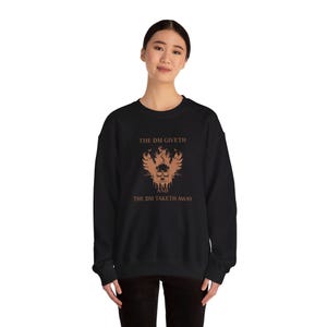 Op de afbeelding: Zwart sweatshirt met een bruine grafische print van een schedel met vleugels en de tekst "The DM Giveth and The DM Taketh Away".