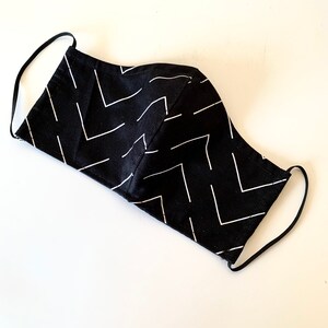 May include: Black face mask with white chevron pattern. The mask has elastic ear loops.