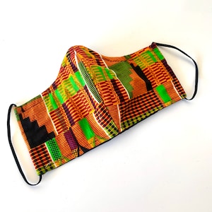 May include: A reusable face mask with a colorful geometric pattern in shades of orange, green, black, and white. The mask has black elastic ear loops.