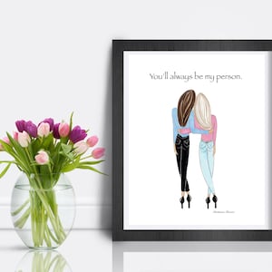K&ouml;nnte beinhalten: Ein gerahmter Druck mit einer Illustration von zwei Figuren, die sich umarmen. Der Text "You'll always be my person" befindet sich &uuml;ber den Figuren. Links befindet sich eine Vase mit rosa und lila Tulpen.