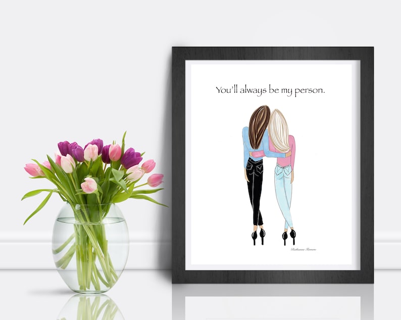 K&ouml;nnte beinhalten: Ein gerahmter Druck mit einer Illustration von zwei Figuren, die sich umarmen. Der Text "You'll always be my person" befindet sich &uuml;ber den Figuren. Links befindet sich eine Vase mit rosa und lila Tulpen.