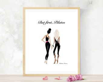 May include: A framed print featuring two stylized figures in workout attire. The figures are in black and pink activewear. The text "But first, Pilates" is above the figures. The print is in a light wood frame.