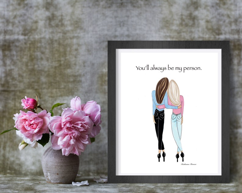 K&ouml;nnte beinhalten: Gerahmter Kunstdruck mit einer Illustration von zwei sich umarmenden Frauen. Der Text "You'll always be my person" steht &uuml;ber der Illustration. Links ist eine Vase mit rosa Blumen.