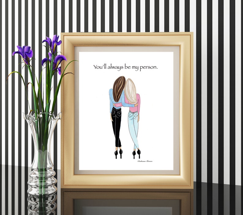 K&ouml;nnte beinhalten: Ein gerahmter Druck in einem goldfarbenen Rahmen zeigt eine Illustration von zwei Figuren, die sich umarmen. Die Figuren tragen Jeans und Oberteile in Blau und Rosa. Der Text "You'll always be my person" steht &uuml;ber den Figuren.