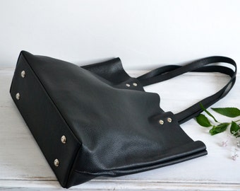 May include: A black leather tote bag with double straps and silver rivets. The bag is lying on a white surface.