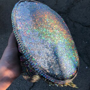 May include: A silver iridescent hat with a sparkly finish. The hat has a rounded crown and a wide brim.
