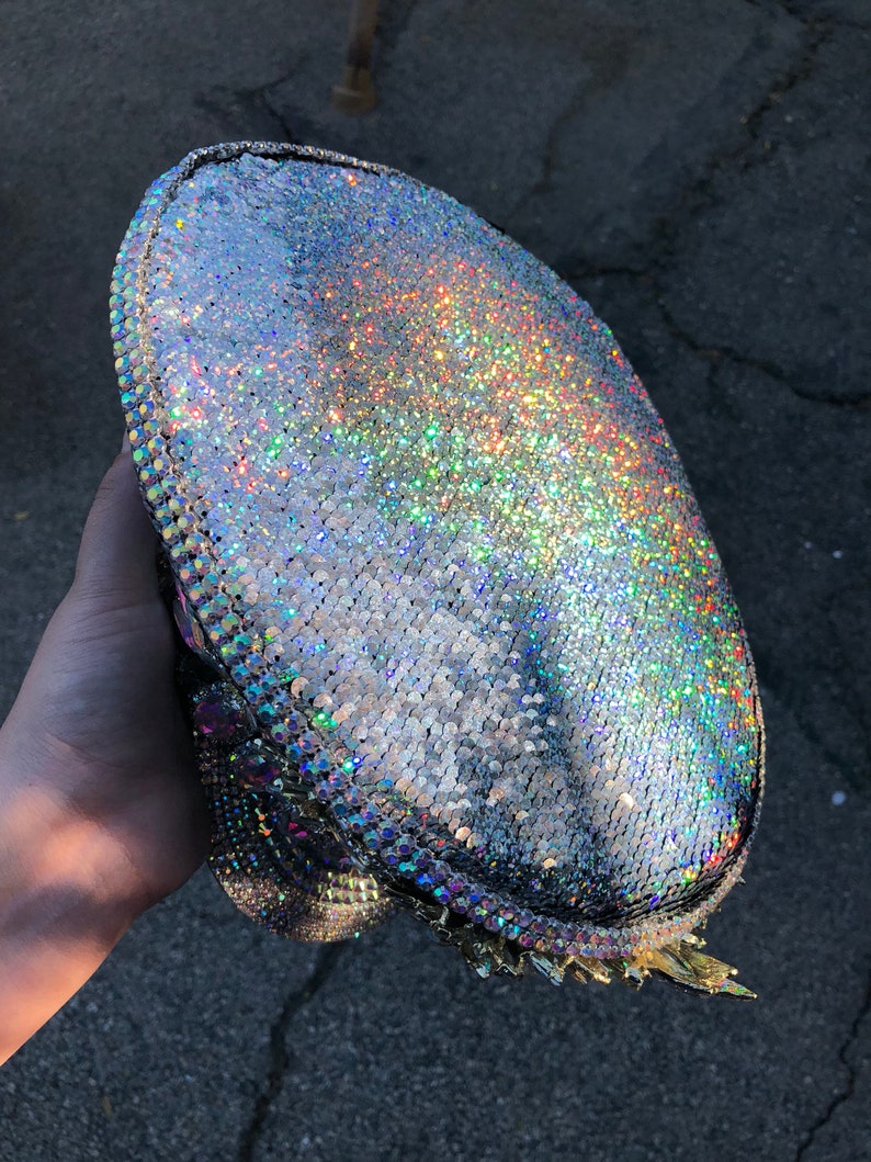 May include: A silver iridescent hat with a sparkly finish. The hat has a rounded crown and a wide brim.