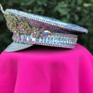 May include: A silver sequined hat with iridescent rhinestones and a white band. The hat is sitting on a pink surface.