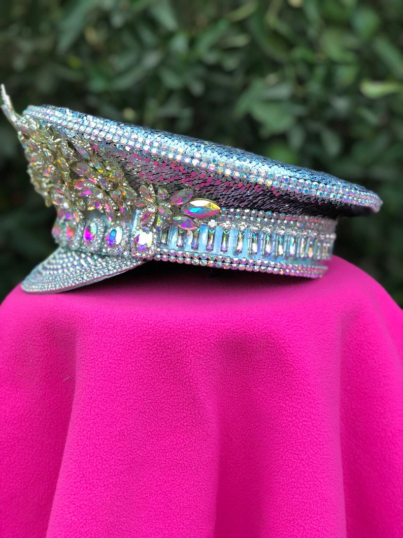 May include: A silver sequined hat with iridescent rhinestones and a white band. The hat is sitting on a pink surface.