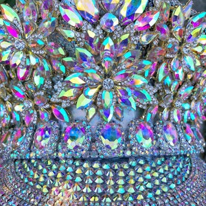 May include: A crown made of iridescent rhinestones and gold-toned metal. The crown is decorated with large, faceted rhinestones in a flower pattern. The crown is also decorated with smaller rhinestones.