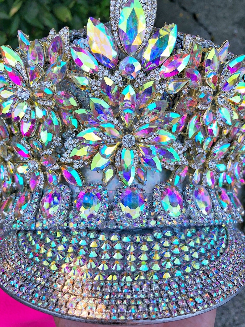 May include: A crown made of iridescent rhinestones and gold-toned metal. The crown is decorated with large, faceted rhinestones in a flower pattern. The crown is also decorated with smaller rhinestones.